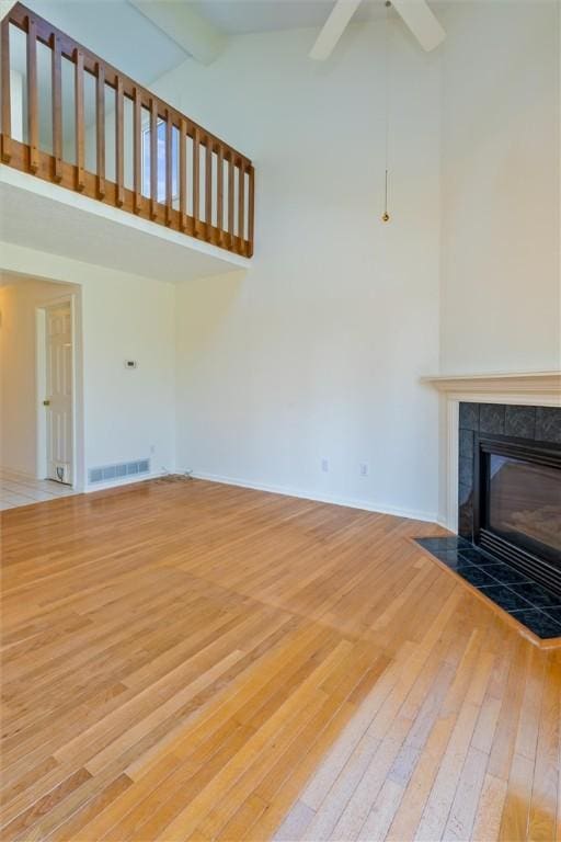 unfurnished living room featuring visible vents, high vaulted ceiling, a tile fireplace, beamed ceiling, and light wood-type flooring