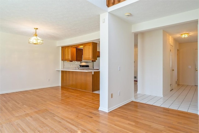 kitchen featuring brown cabinets, light wood-style flooring, decorative light fixtures, an inviting chandelier, and light countertops