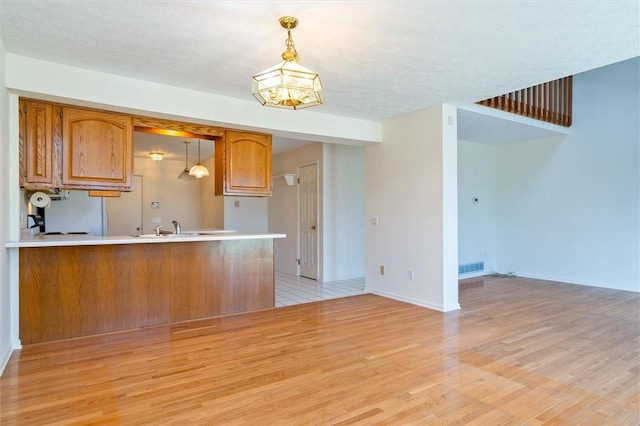 kitchen featuring light countertops, light wood-style flooring, brown cabinetry, and hanging light fixtures