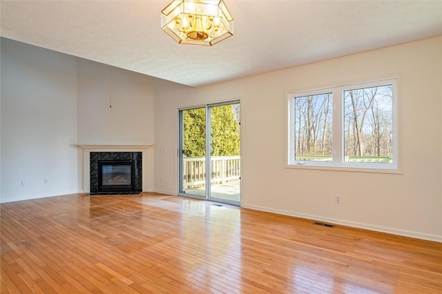 unfurnished living room with visible vents, a notable chandelier, hardwood / wood-style floors, a premium fireplace, and baseboards