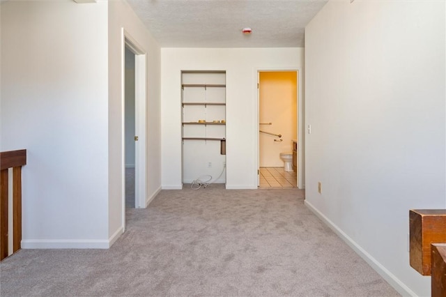 unfurnished bedroom with connected bathroom, a textured ceiling, baseboards, and carpet floors