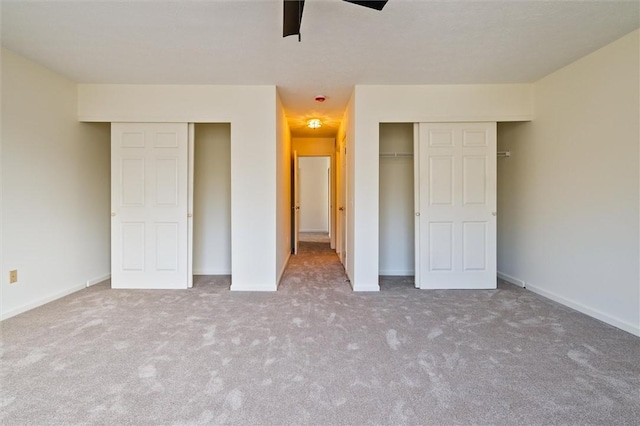 unfurnished bedroom with a ceiling fan, carpet, baseboards, and multiple closets