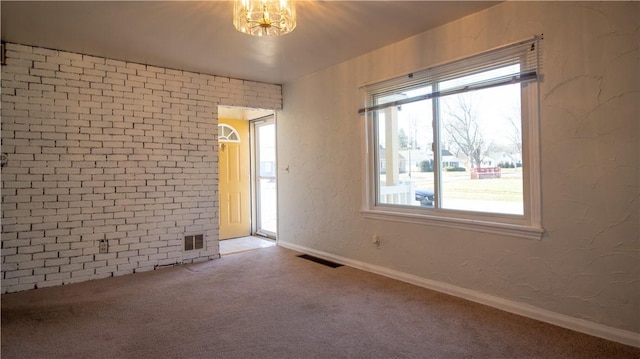 carpeted empty room with visible vents, brick wall, baseboards, and a textured wall