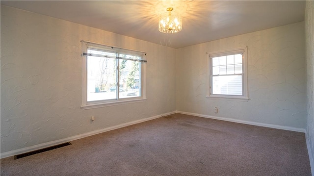 carpeted spare room featuring baseboards, visible vents, plenty of natural light, and an inviting chandelier