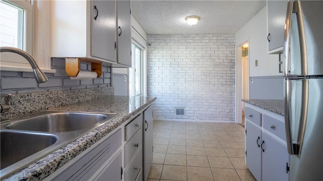 kitchen with visible vents, a sink, a textured ceiling, freestanding refrigerator, and light tile patterned floors