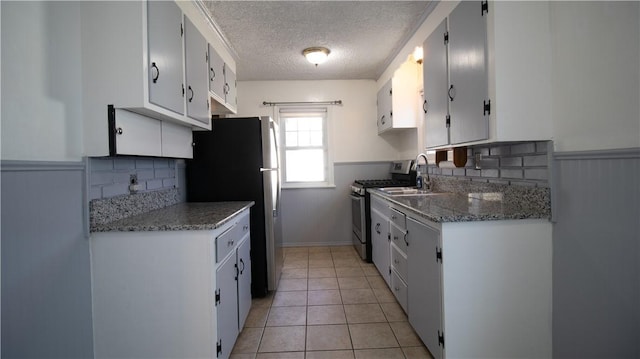 kitchen with a sink, stainless steel appliances, a wainscoted wall, and light tile patterned flooring