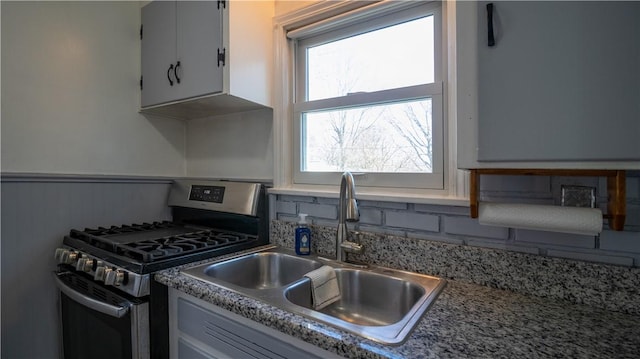 kitchen with a sink, a wainscoted wall, stainless steel range with gas stovetop, and decorative backsplash