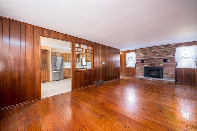 unfurnished living room with a fireplace, wooden walls, light wood-style floors, and visible vents