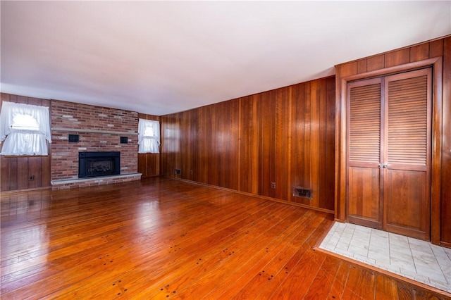 unfurnished living room featuring visible vents, wood walls, a brick fireplace, and wood-type flooring