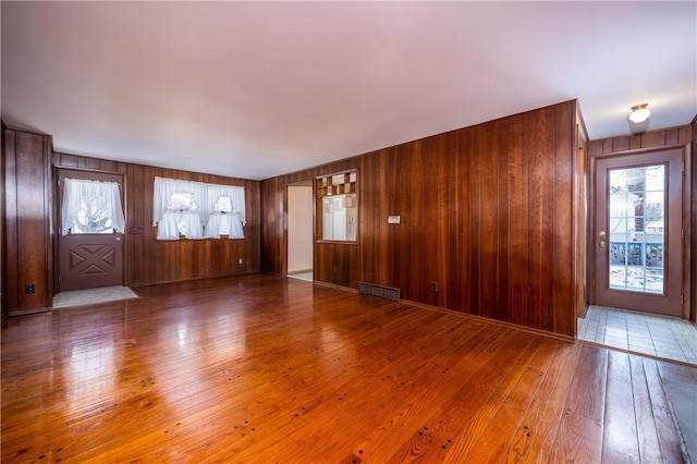 unfurnished living room featuring hardwood / wood-style floors, visible vents, and wood walls