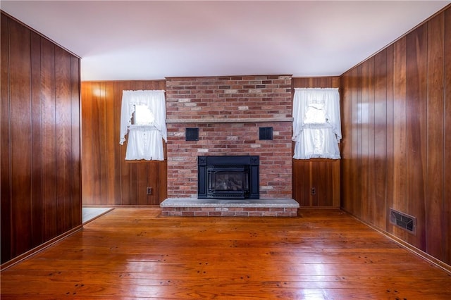 unfurnished living room featuring a brick fireplace, visible vents, wood-type flooring, and wood walls