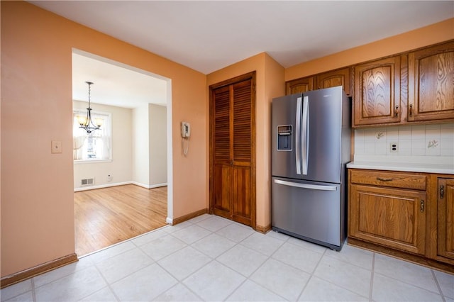 kitchen with brown cabinetry, tasteful backsplash, visible vents, and stainless steel refrigerator with ice dispenser