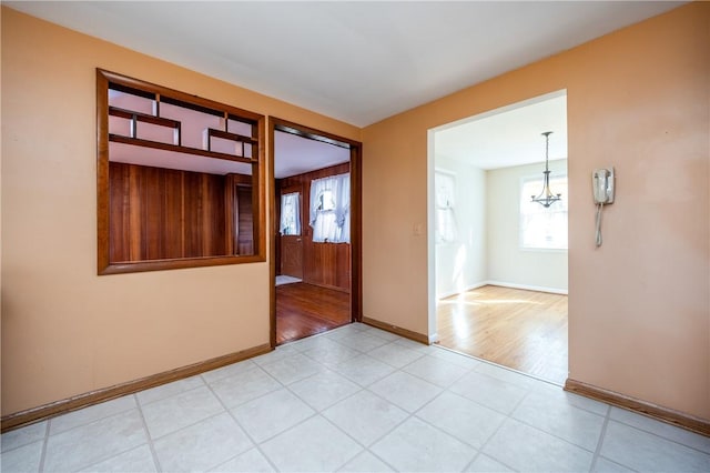 empty room featuring light tile patterned floors, a chandelier, and baseboards