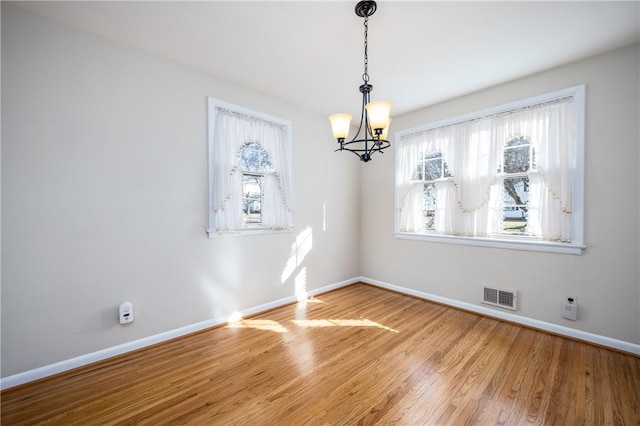 unfurnished dining area with a notable chandelier, wood finished floors, visible vents, and baseboards