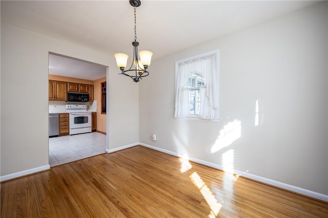 unfurnished dining area with an inviting chandelier, baseboards, and light wood-style floors