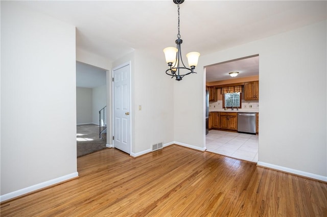 unfurnished dining area featuring light wood-type flooring, visible vents, baseboards, and a notable chandelier