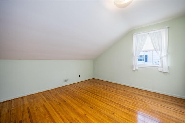 bonus room featuring visible vents, light wood-style floors, baseboards, and vaulted ceiling