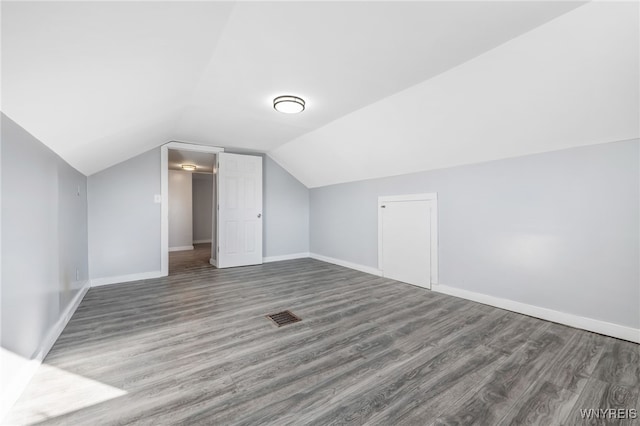 additional living space with vaulted ceiling, wood finished floors, visible vents, and baseboards