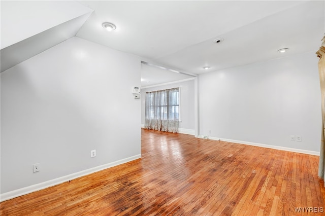 unfurnished room featuring baseboards, light wood-style floors, and lofted ceiling