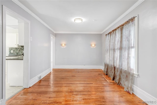 empty room with a sink, baseboards, light wood-style floors, and ornamental molding