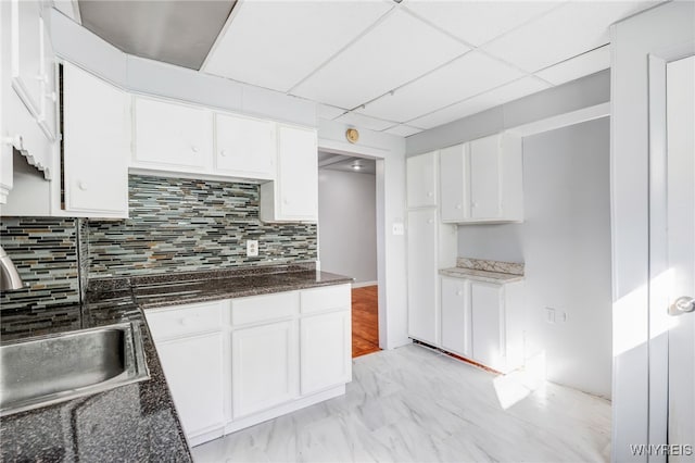 kitchen featuring a sink, decorative backsplash, a paneled ceiling, and white cabinetry