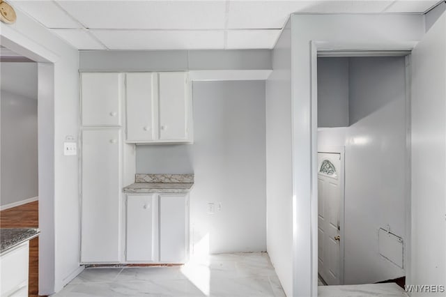 kitchen featuring light countertops, white cabinets, marble finish floor, and a drop ceiling