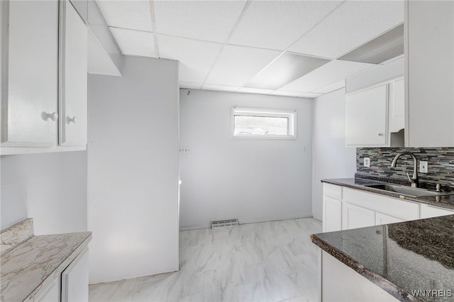 kitchen with a sink, white cabinetry, dark stone counters, decorative backsplash, and a paneled ceiling