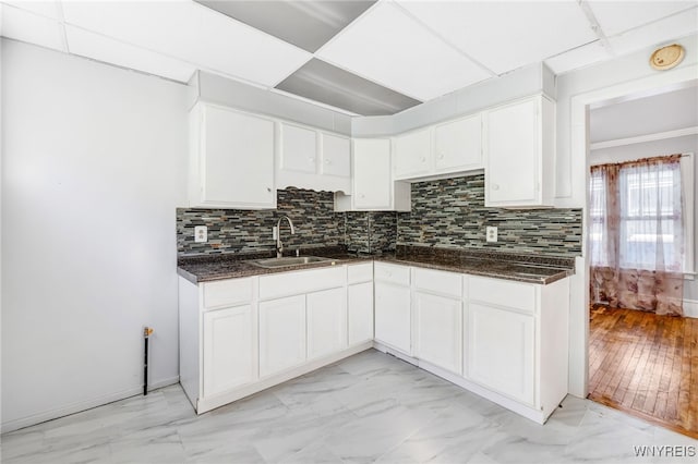 kitchen featuring tasteful backsplash, marble finish floor, white cabinets, and a sink