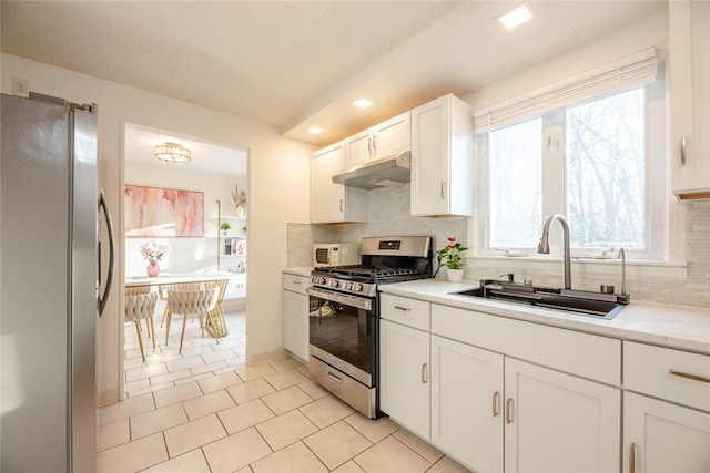 kitchen with a sink, under cabinet range hood, appliances with stainless steel finishes, white cabinets, and light countertops