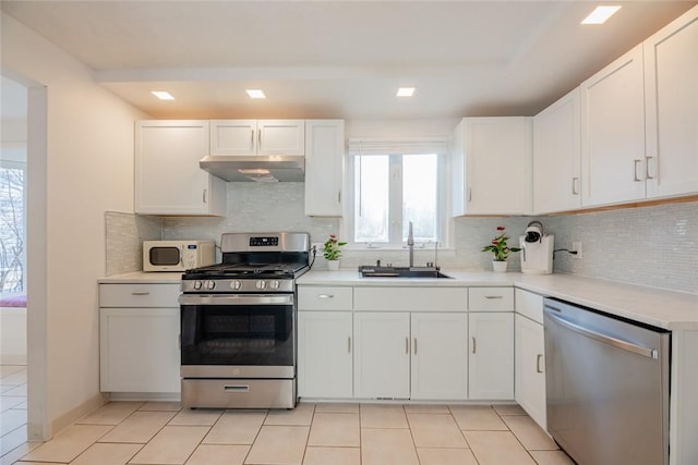 kitchen with under cabinet range hood, appliances with stainless steel finishes, plenty of natural light, white cabinetry, and a sink