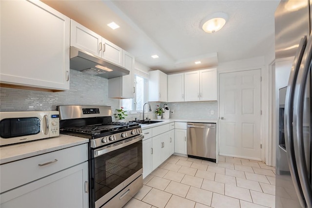 kitchen with under cabinet range hood, a sink, appliances with stainless steel finishes, white cabinets, and light countertops