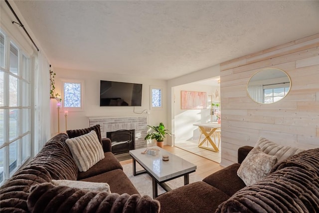 living area featuring wooden walls, a brick fireplace, wood finished floors, and a textured ceiling