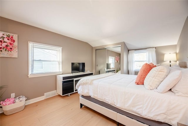 bedroom featuring visible vents, baseboards, light wood-type flooring, lofted ceiling, and a closet