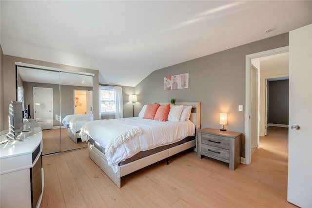 bedroom featuring light wood-type flooring, lofted ceiling, and a closet