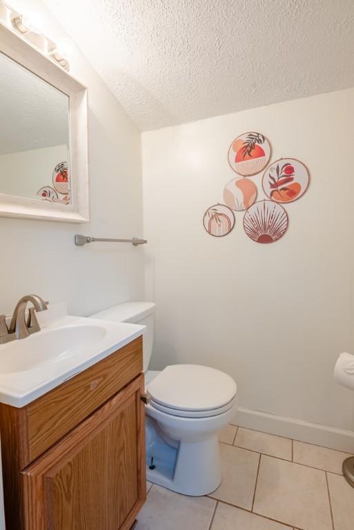 half bathroom featuring tile patterned floors, toilet, vanity, and a textured ceiling