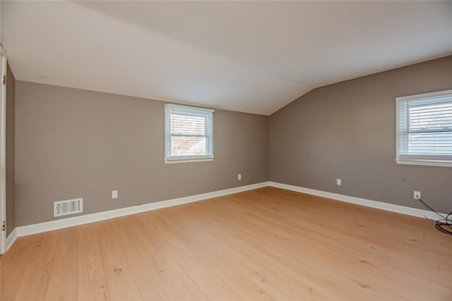 additional living space with visible vents, light wood-style flooring, a healthy amount of sunlight, and vaulted ceiling