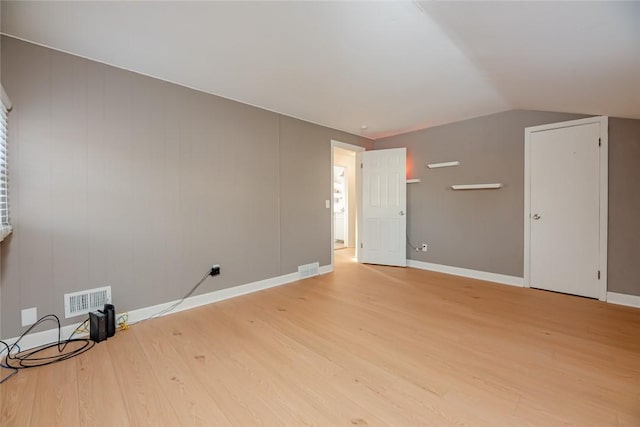 spare room with light wood finished floors, visible vents, baseboards, and vaulted ceiling