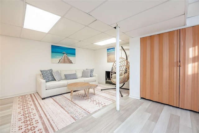 living area featuring baseboards, a paneled ceiling, and light wood finished floors