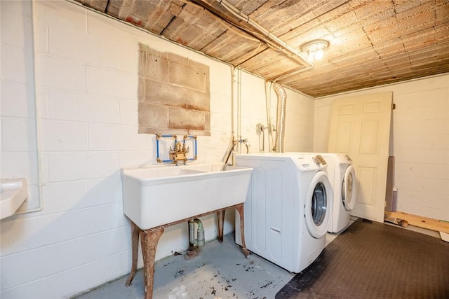 clothes washing area featuring a sink, laundry area, concrete block wall, and washer and clothes dryer