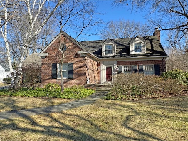 cape cod-style house featuring brick siding, a chimney, and a front lawn