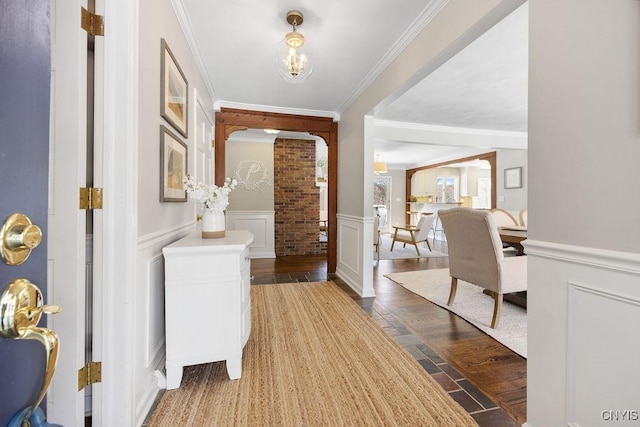 foyer entrance featuring crown molding, a decorative wall, wood finished floors, and a wainscoted wall