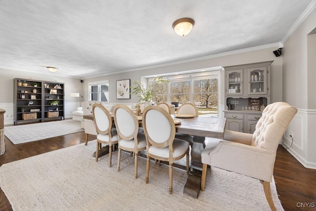 dining room with a wainscoted wall, a decorative wall, wood finished floors, and ornamental molding