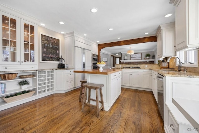 kitchen featuring a sink, a peninsula, appliances with stainless steel finishes, white cabinets, and glass insert cabinets