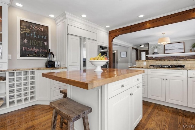 kitchen featuring dark wood-type flooring, a breakfast bar area, ornamental molding, appliances with stainless steel finishes, and white cabinets