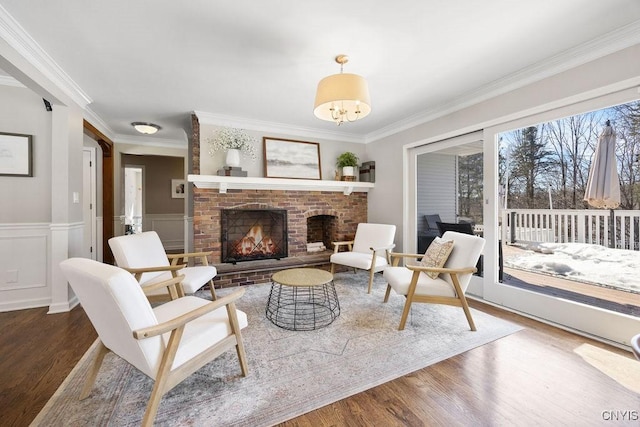 living room with a wainscoted wall, a brick fireplace, wood finished floors, and crown molding