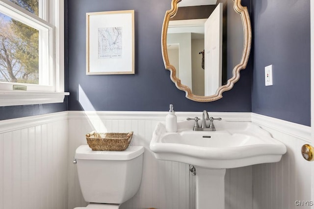 half bath featuring toilet and a wainscoted wall