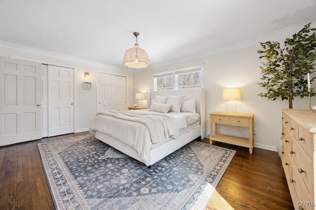 bedroom featuring baseboards, multiple closets, dark wood finished floors, and crown molding