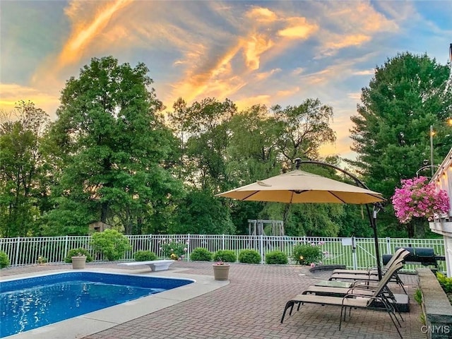 pool at dusk with a diving board, a fenced in pool, a patio, and fence