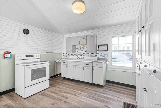 kitchen with white electric stove, visible vents, light wood-style floors, and brick wall