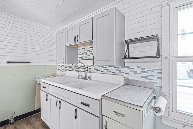 kitchen featuring light countertops, dark wood-style floors, tasteful backsplash, and brick wall